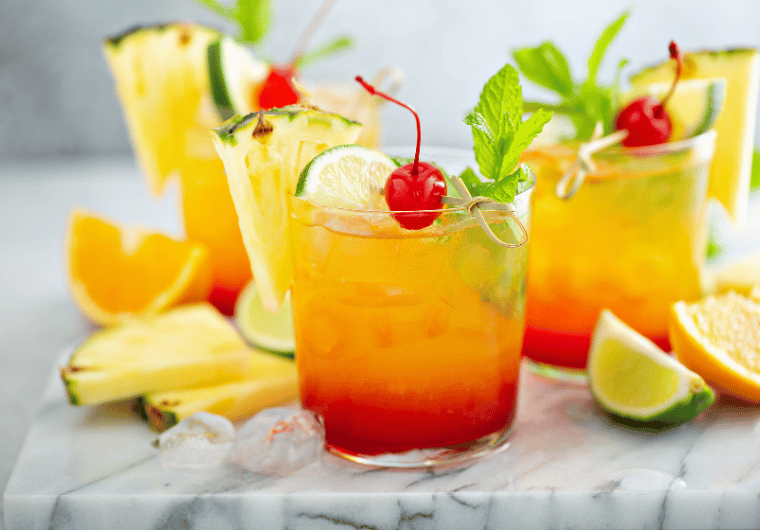 Tequila Sunrise mocktail with layers of orange and red, garnished with pineapple, lime, and cherry | Angelia Mendoza