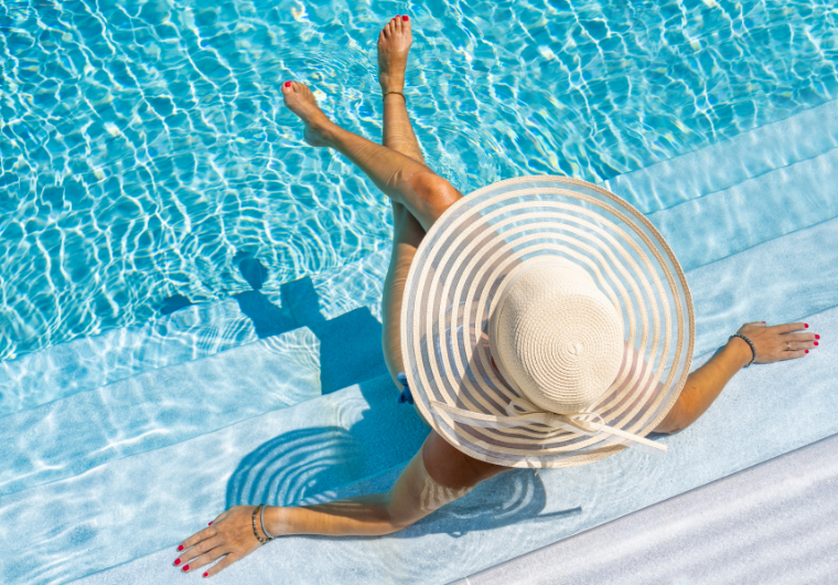 Woman relaxing by a pool in a wide-brim hat, representing a simple, stress-free way to get rich and enjoy financial freedom. | Angelia Mendoza