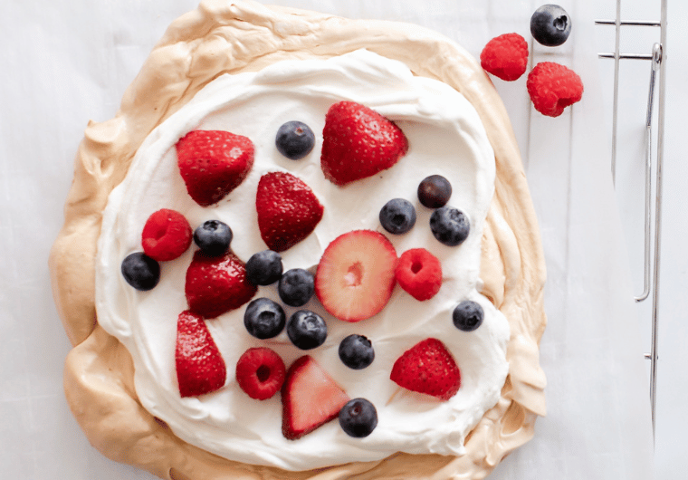 Overhead shot of a meringue dessert topped with whipped cream, strawberries, blueberries, and raspberries—highlighting common nutritional mistakes related to sugar and portion control.