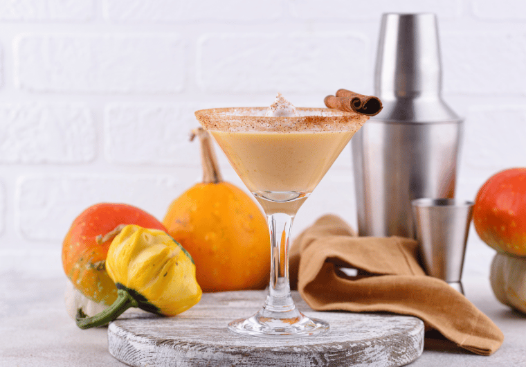Pumpkin martini cocktail surrounded by gourds and fall decor, representing cozy fall bucket list activities for adults.