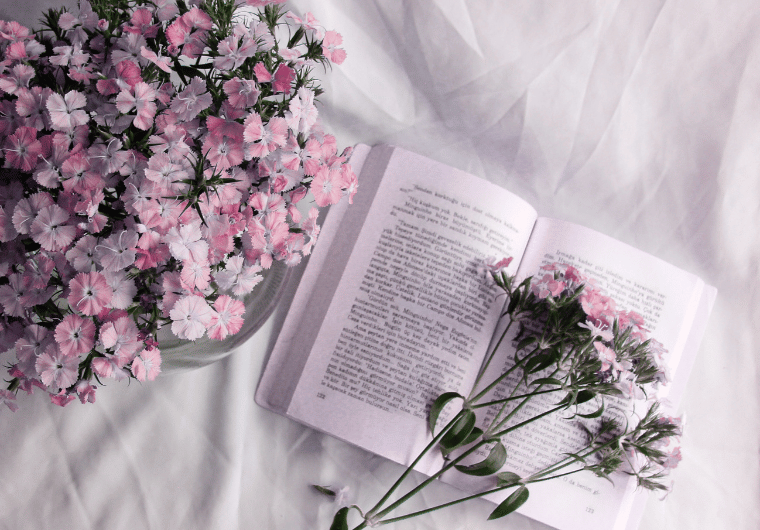 Open book with lavender pages and delicate pink flowers arranged on soft white fabric, symbolizing self-care, mindfulness, and the joy of reading for women over 50.