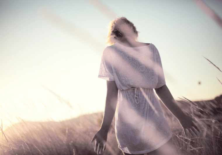 Woman standing in a sunlit field with arms relaxed, embracing peace and presence—symbolizing aging gracefully with joy and freedom.