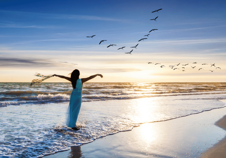 Silhouette of a woman standing with arms outstretched at sunset, symbolizing freedom and empowerment.