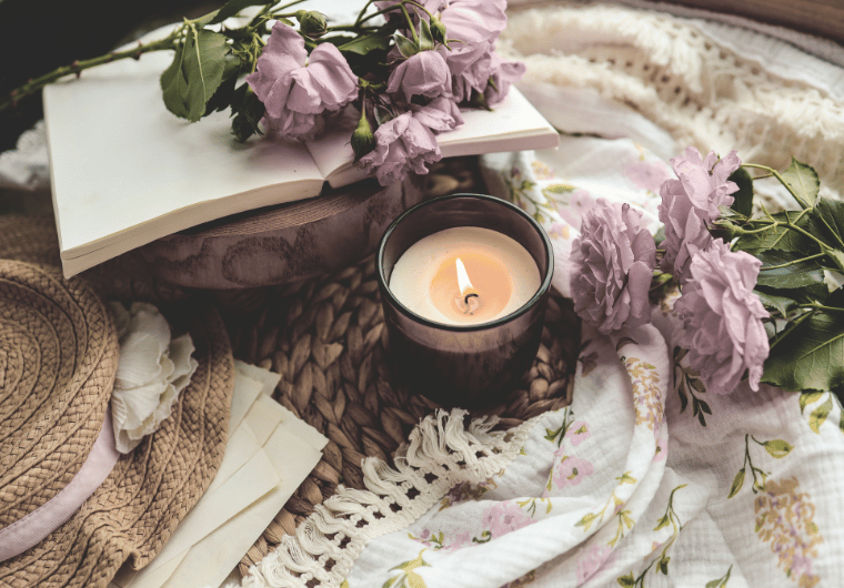 Soft pink flowers, an open book, a candle, and cozy textures arranged on a woven mat—creating a peaceful, reflective space for healing and self-care. | Angelia Mendoza