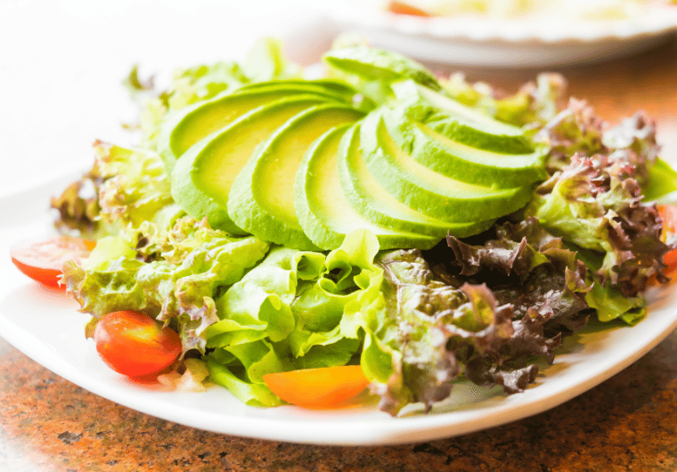 Plate of fresh green salad topped with perfectly sliced ripe avocado, cherry tomatoes, and mixed greens. | Angelia Mendoza
