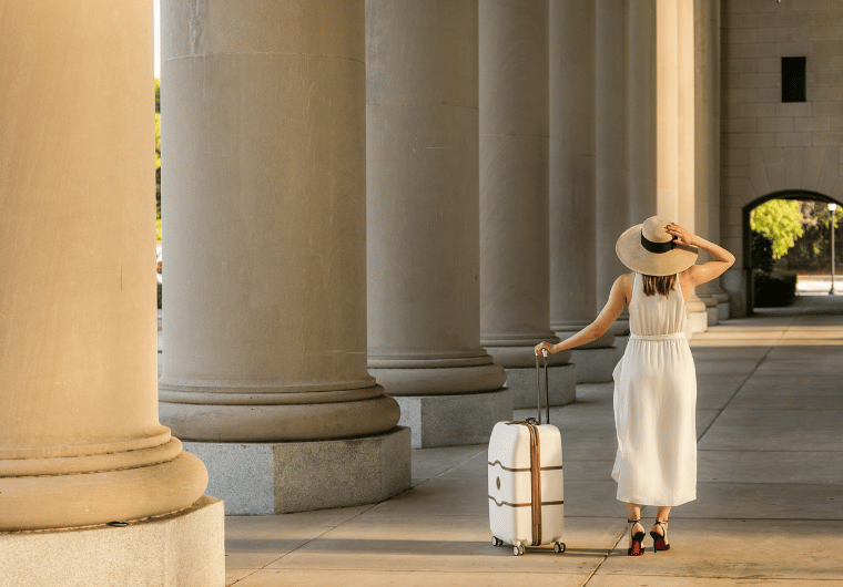 Woman in a white dress and sunhat walking away with a suitcase, symbolizing leaving an unhappy marriage and starting a new chapter in life.