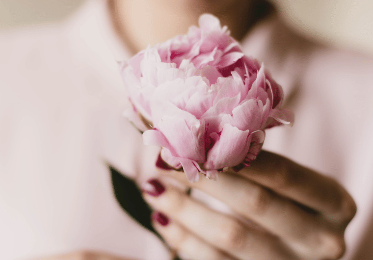 Close-up of a woman holding a pink peony flower gently in her hands, symbolizing softness and inner healing. | Angelia Mendoza