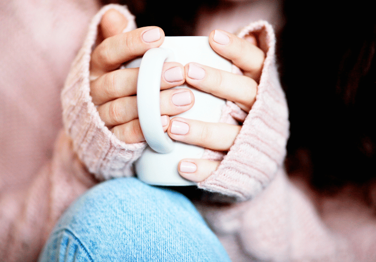 Hands in a cozy pink sweater holding a white mug, symbolizing comfort and quiet self-care. | Angelia Mendoza
