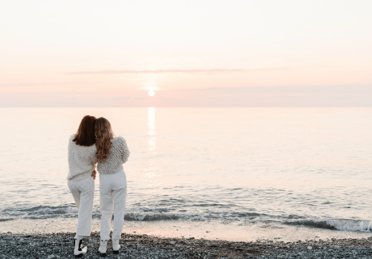 Two women standing together on a beach at sunset, offering comfort and support, symbolizing healing and finding connection after leaving an unhappy marriage.
