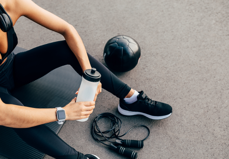 Woman in affordable workout clothes resting on a mat with water bottle, jump rope, and medicine ball. | Angelia Mendoza