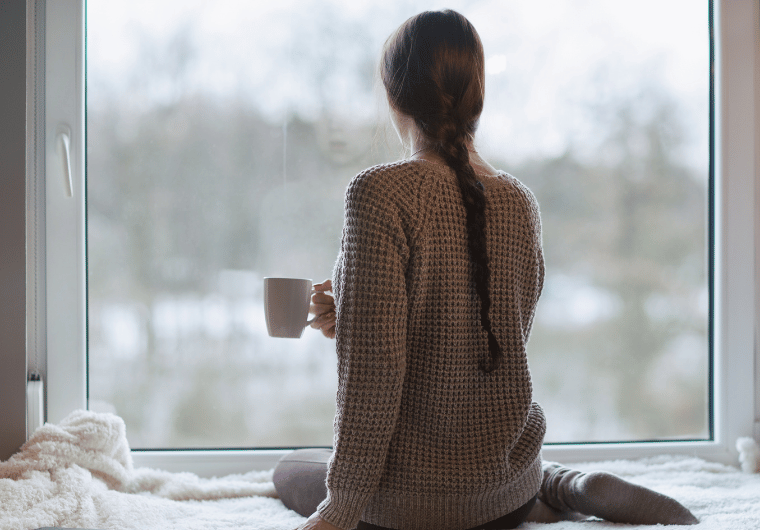 Woman holding a mug and looking out a window—symbolizing managing anxiety and depression through quiet reflection | Angelia Mendoza